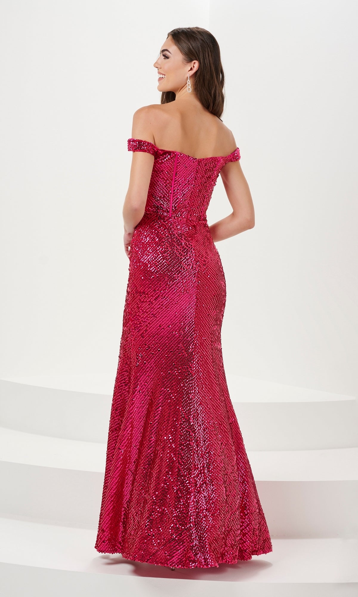 A woman stands on white steps, facing away, in the Off-the-Shoulder Long Sequin Prom Dress 14158 with a corset bodice and floor-length bright pink skirt.